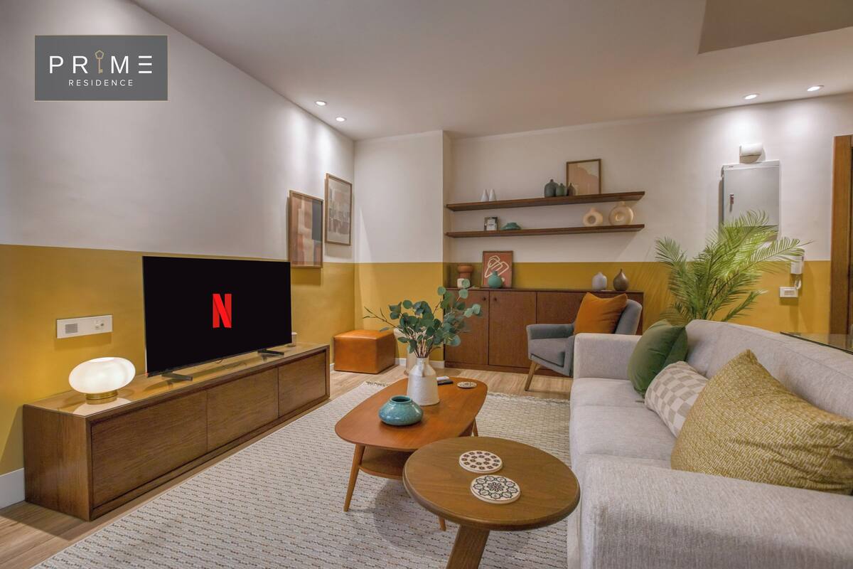 Een moderne woonkamer met een flatscreen televisie, houten meubels, een bank, een salontafel en decoratieve objecten.