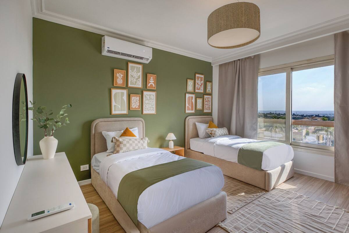 Een hotelkamer met twee bedden, een televisie, een plant, kunst aan de muur en uitzicht op de stad.