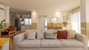 A living room with a sofa, a dining table, and a kitchen in the background. - Prime Residence Golf Kattameya (Shurtah al-Dakhlah)