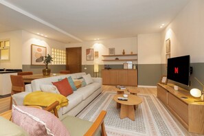 Una sala moderna con sofá, mesa de centro, televisor y un área de cocina al fondo.