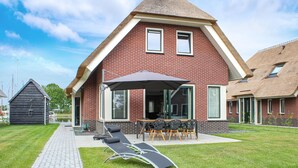 A red brick house with a large patio, outdoor seating, and a thatched-roof structure.