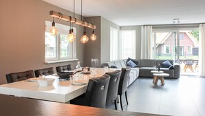 A modern kitchen with a dining area, featuring a large table, chairs, a built-in oven, and pendant lighting.