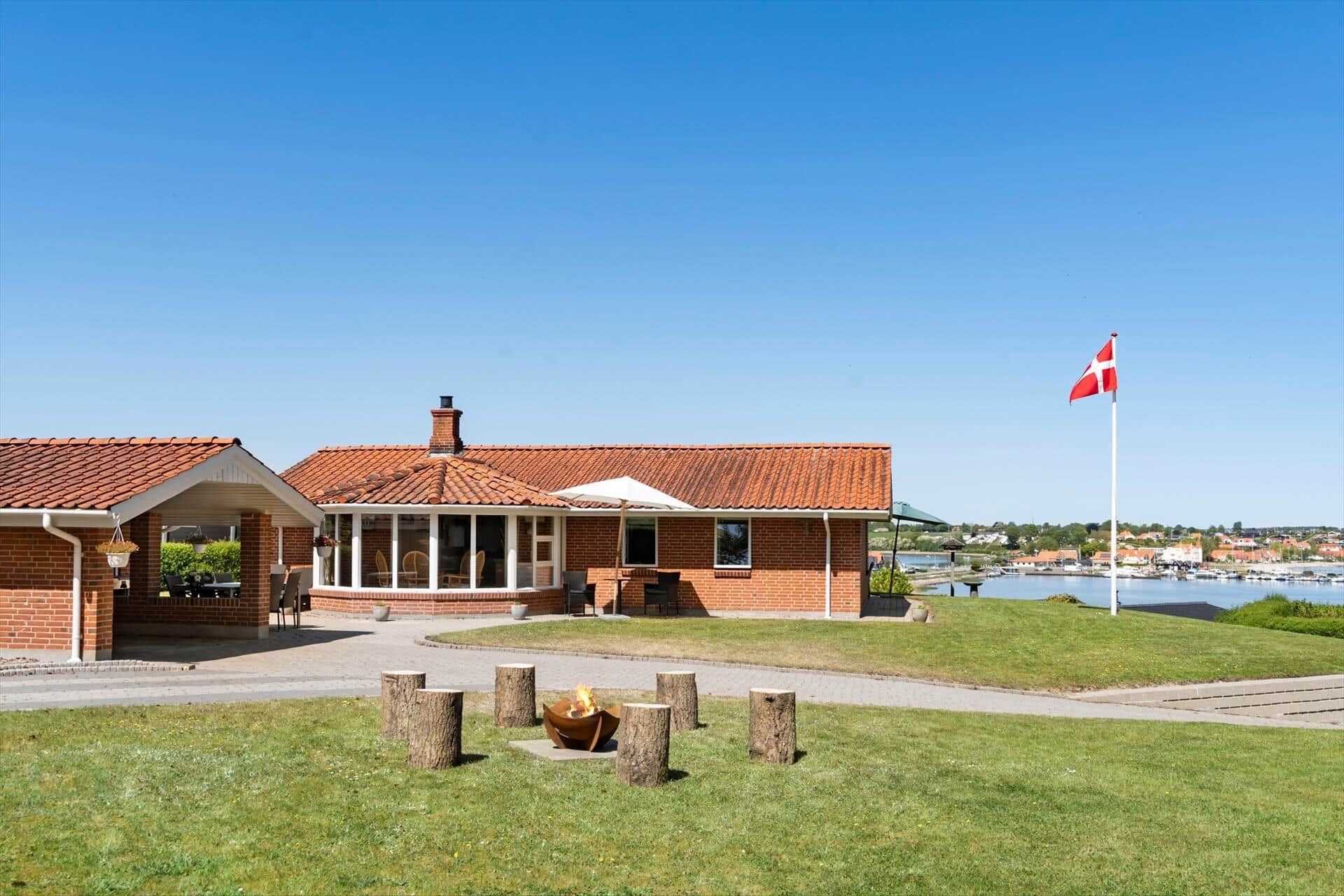 A brick building with a tiled roof, a flagpole with a flag, and a grassy area with wooden stumps.