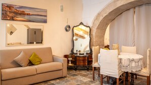 Una habitación acogedora con un sofá color beige, una mesa de madera con mantel de encaje y un espejo grande.