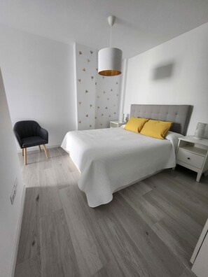 Ein Schlafzimmer mit einem Bett, einem Sessel, einem Nachttisch und einer Wand mit Blattmustern.