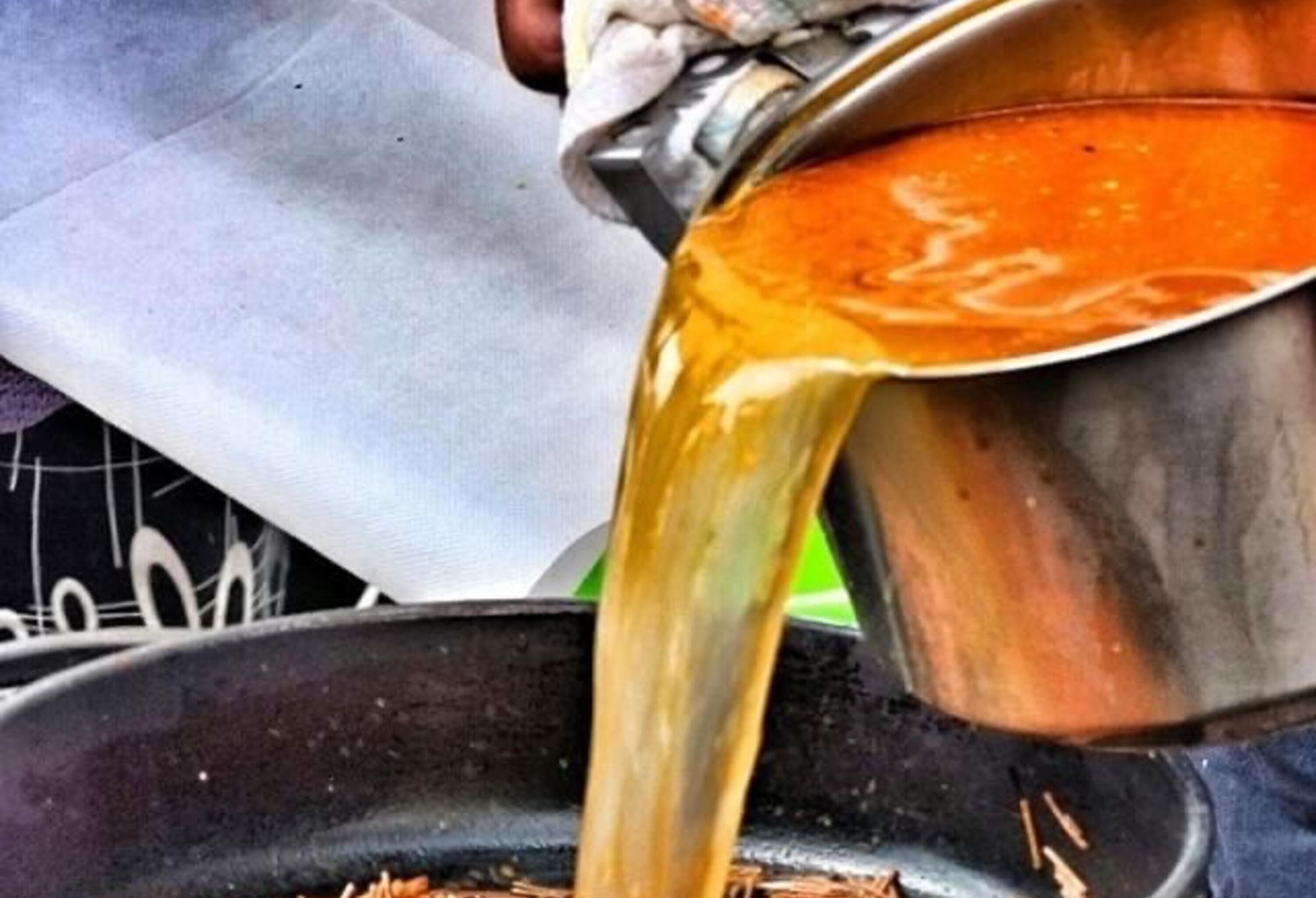 A person pouring a liquid from a metal container into a black pan.