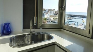 A kitchen with a stainless steel sink, a blue vase, and a view of a coastal town through a window.