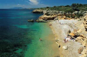 A coastal beach with clear turquoise water, rocky terrain, and people sunbathing.