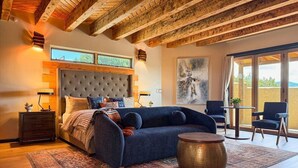A modern bedroom with a large bed, a blue sofa, a round coffee table, and a view of the outdoors. - Indoor Pool and Pickleball Estate (Santa Fe)