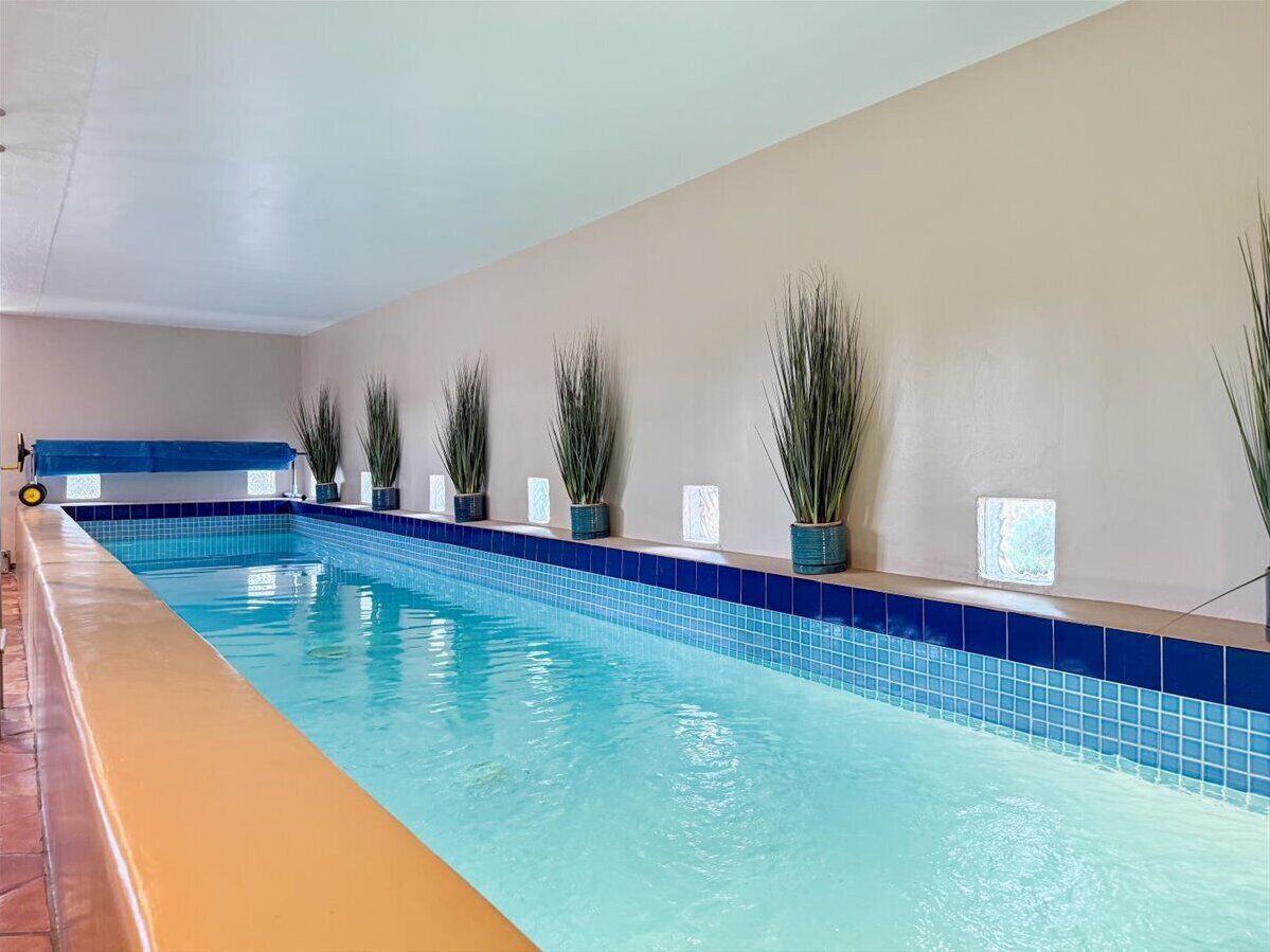 Ein weitläufiger, überdachter Schwimmbereich mit blauen Fliesen, Pflanzen in Töpfen entlang der Wand.