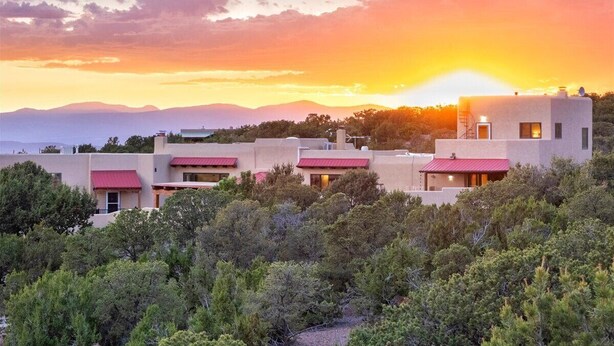 A modern building complex with multiple structures, surrounded by dense greenery and a sunset in the background. - Indoor Pool and Pickleball Estate (Santa Fe)