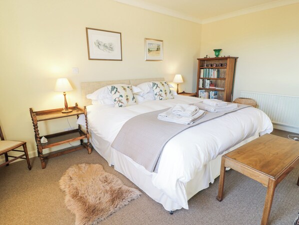 A neatly arranged bedroom with a large bed, bedside tables, a wooden nightstand, a small chair, a fur rug, a wooden bench, and a bookshelf.