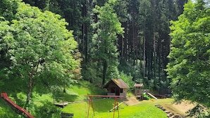 A playground with swings, a slide, and a small wooden structure in a forested area. - Hoferpeterhof: Apartment '1 Room' with Mountain View, Shared Terrace & Wi-Fi (Bad Peterstal-Griesbach)