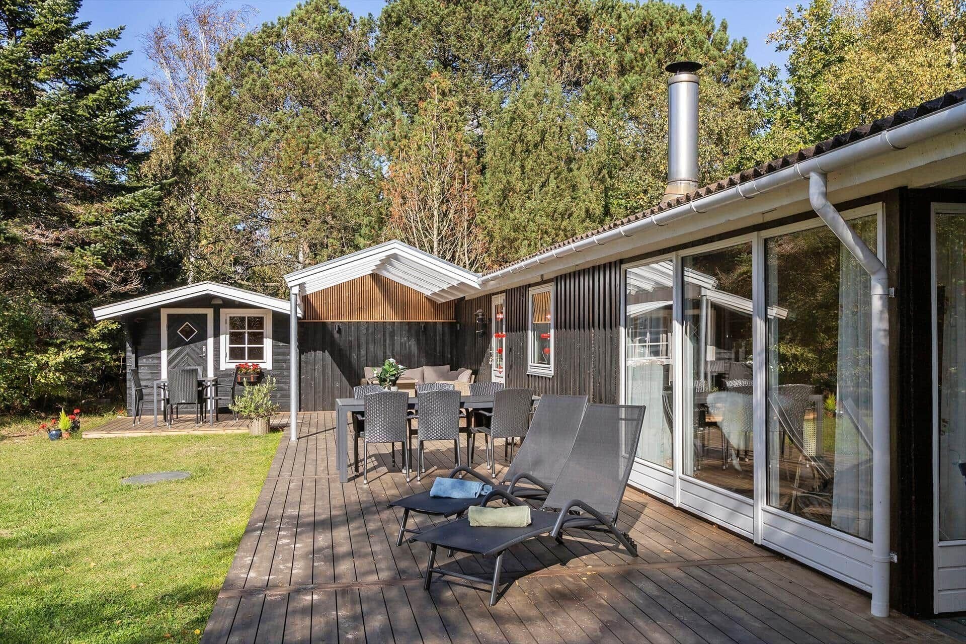 Een modern terras buiten, met een eethoek en lounge stoelen, omringd door een houten terras en een patio met glazen wanden.