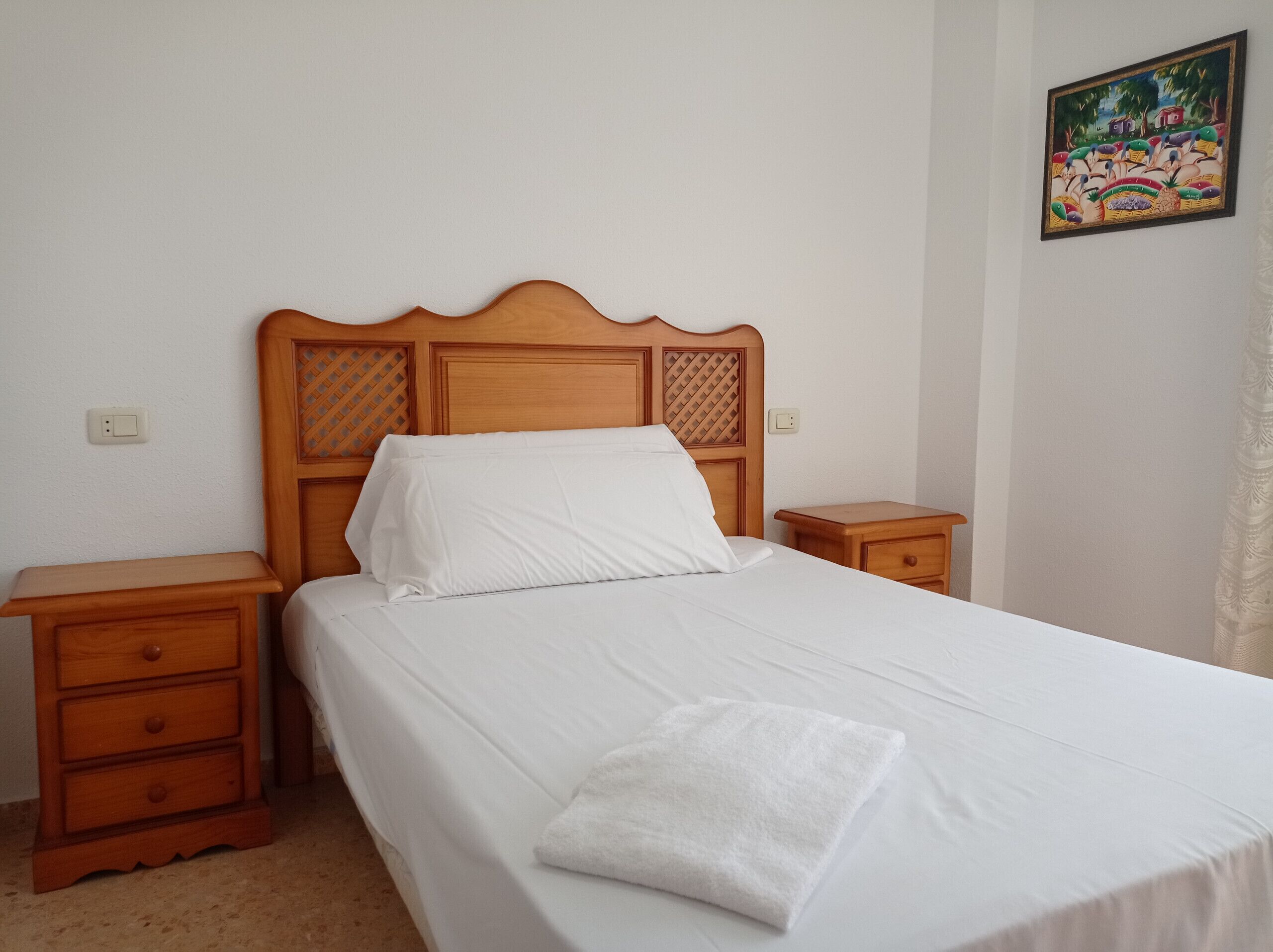 A neatly made bed with white linens and a wooden headboard, flanked by two wooden nightstands with drawers.