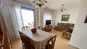 A dining area with a table and chairs, a television, and a sofa in a living room. - PERLA III bl.I 6º ático Solo Familias! (Xeraco Playa)