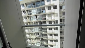 Une vue d’un immeuble résidentiel à plusieurs étages, doté de balcons et d’une rambarde en métal, avec un ciel dégagé.