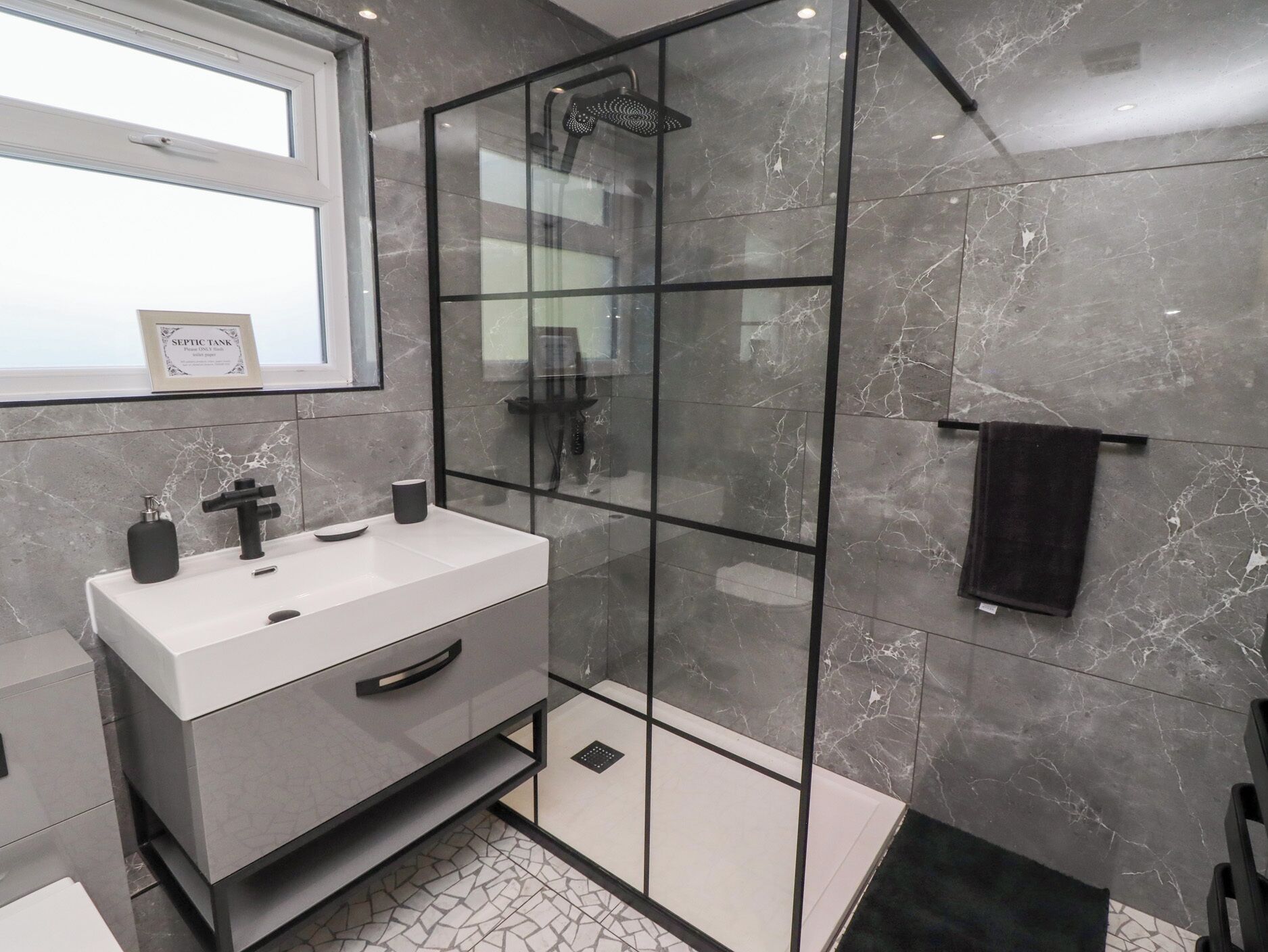A modern bathroom with a glass-enclosed shower, a white sink with a black faucet, and a towel rack with a black towel.