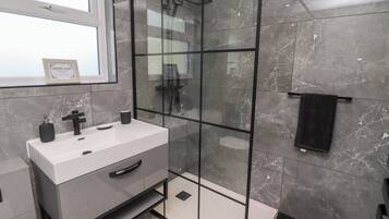A modern bathroom with a glass-enclosed shower, a white sink with a black faucet, and a towel rack with a black towel.