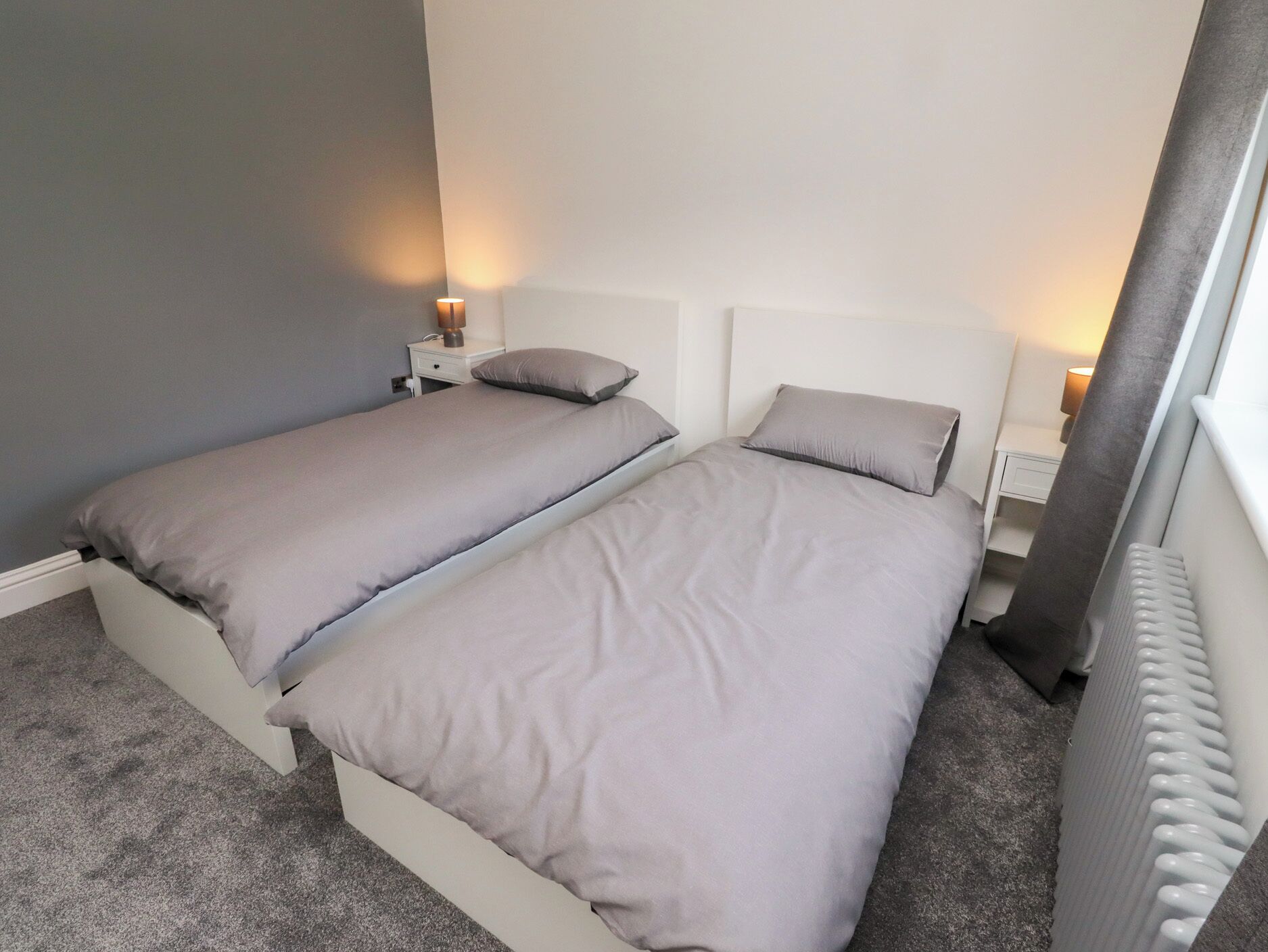 A twin room with two single beds, bedside tables with lamps, and a radiator.