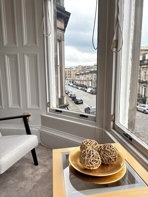 A room with a view of a street, a white chair, a table with a woven ball, and a window with a curtain. - Beautiful Edinburgh apartment - 10 minutes walk from the center (Edinburgh)