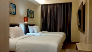 A hotel room with two beds, a large window with curtains, a flat-screen TV, and artwork on the walls. - Caspella Suites Hotel Kemayoran (Jakarta)