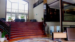 A hotel lobby with a grand staircase, a reception desk, and a large window offering a view of the outdoors. - Caspella Suites Hotel Kemayoran (Jakarta)