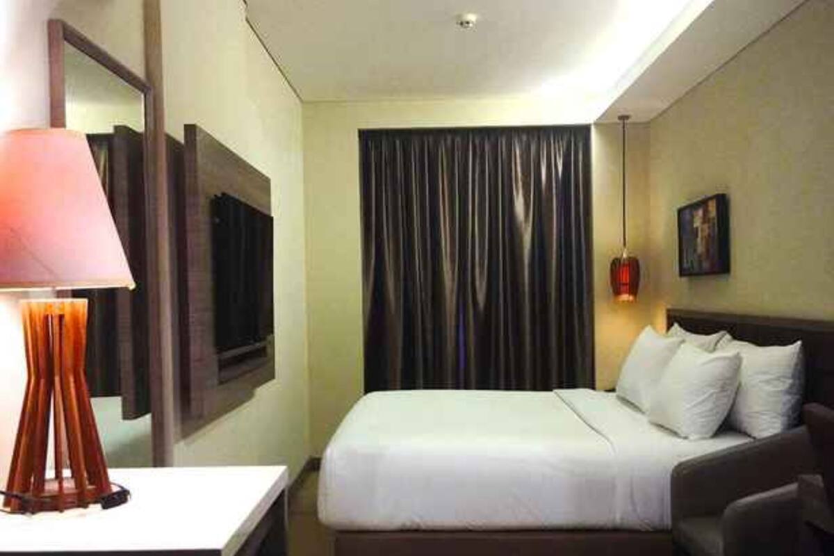 A hotel room with a bed, a desk with a lamp, a TV, a curtain, and a painting on the wall.