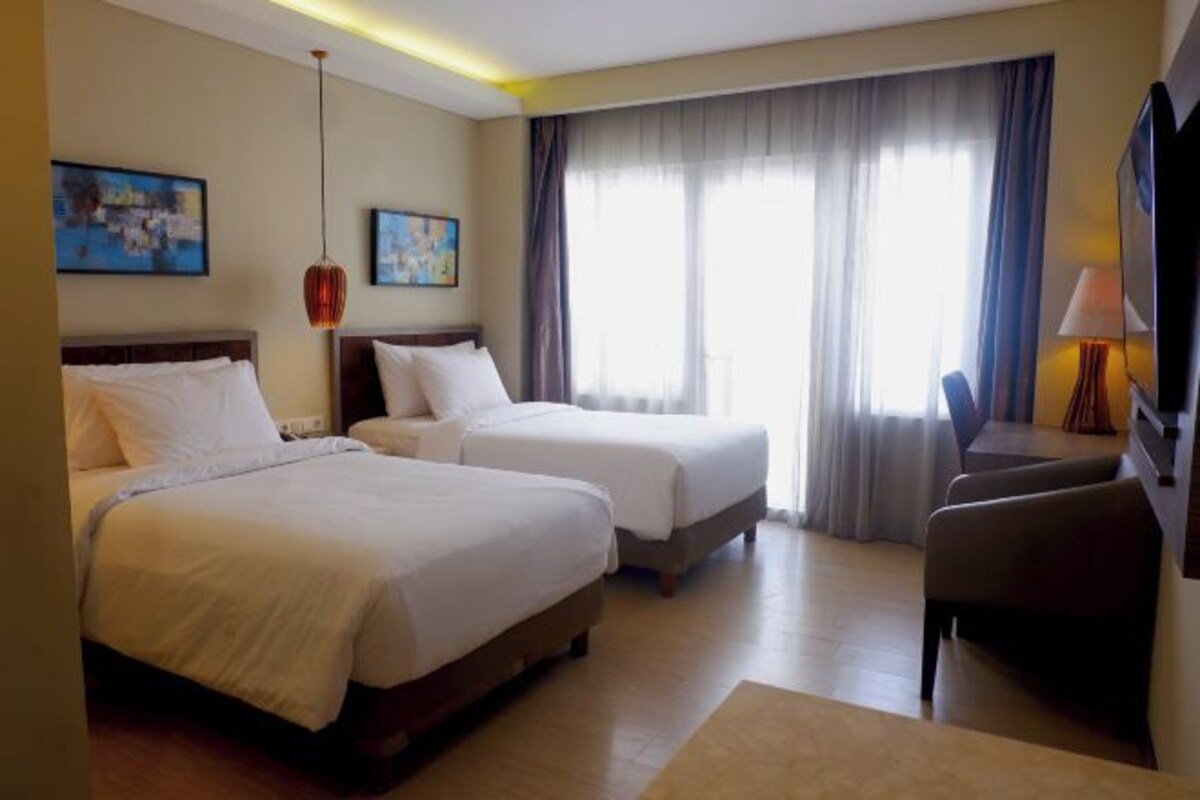 A hotel room with two beds, a desk, a chair, and a large window with curtains.