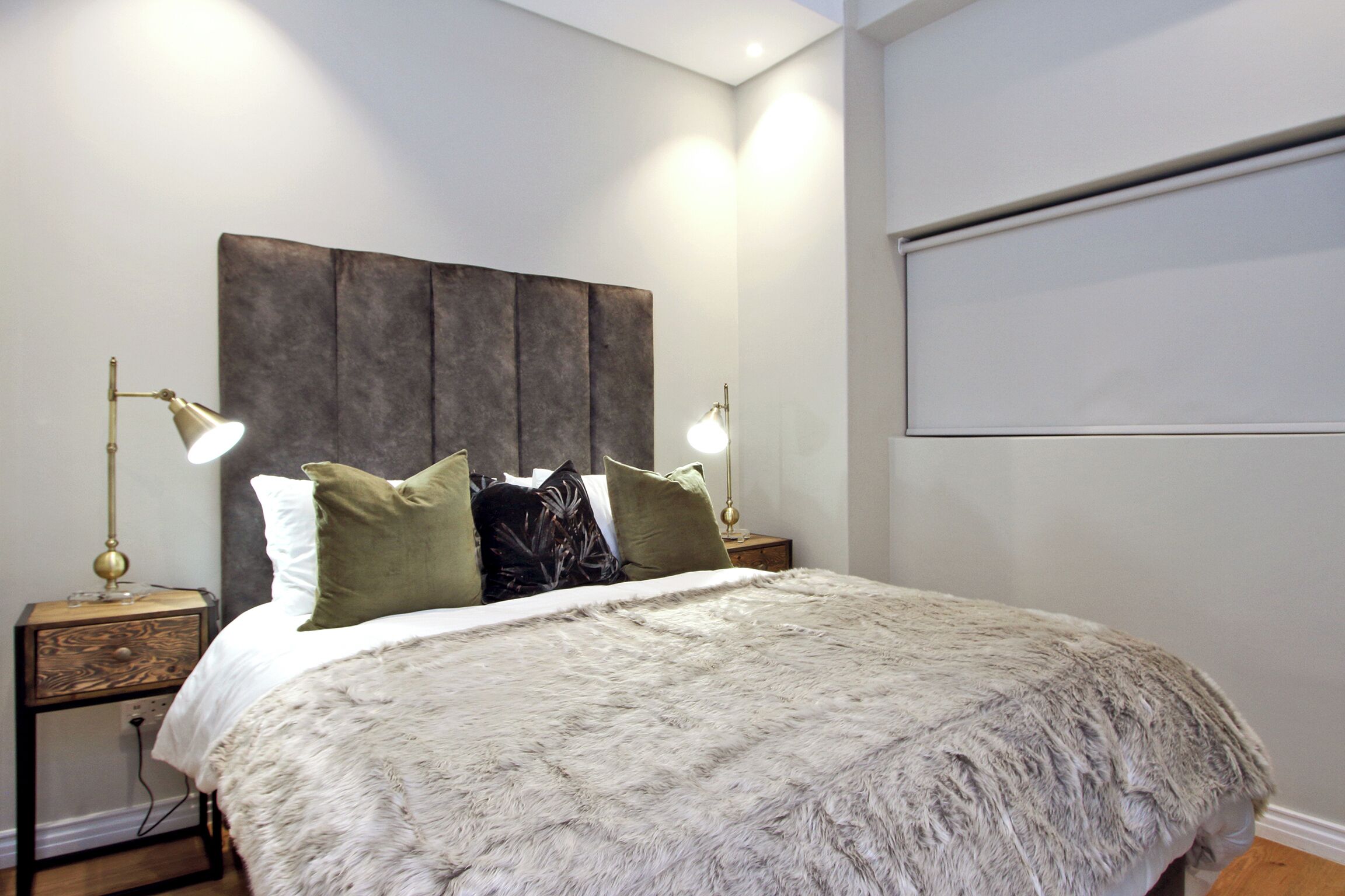 Un dormitorio con una cama grande, dos lámparas de noche, una mesita de madera y un cabecero.