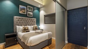 A bedroom with a large bed, a nightstand, a dark door, and framed pictures on the wall. - The Docklands Luxury Apartments (Cape Town)