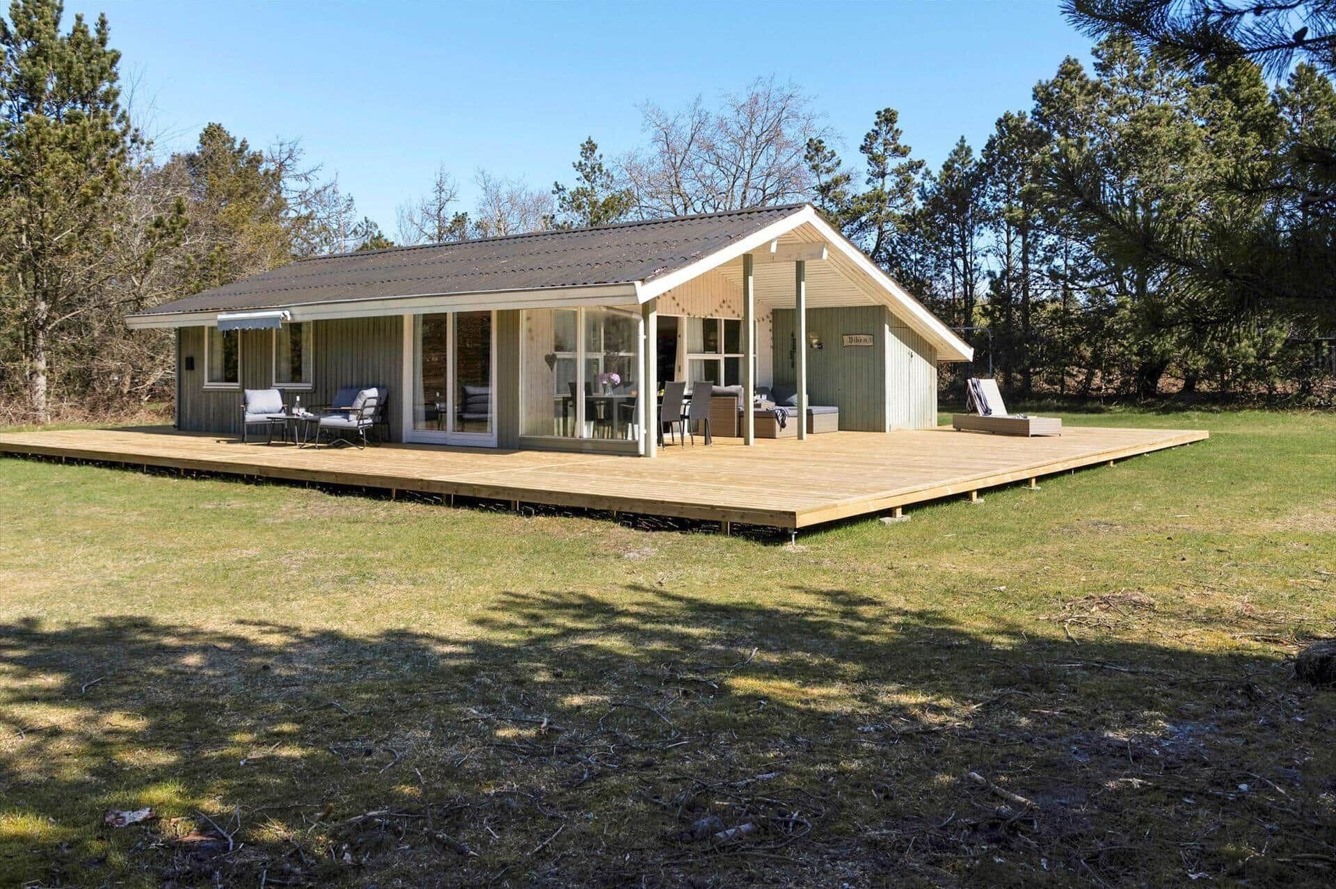 A modern cabin with a deck, large windows, and outdoor seating.