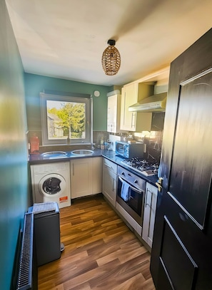 Cocina compacta con lavadora, horno, microondas y ventana con vistas al verdor.