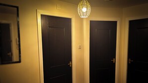 Un couloir avec trois portes en bois sombre, un luminaire suspendu et un plancher en bois.