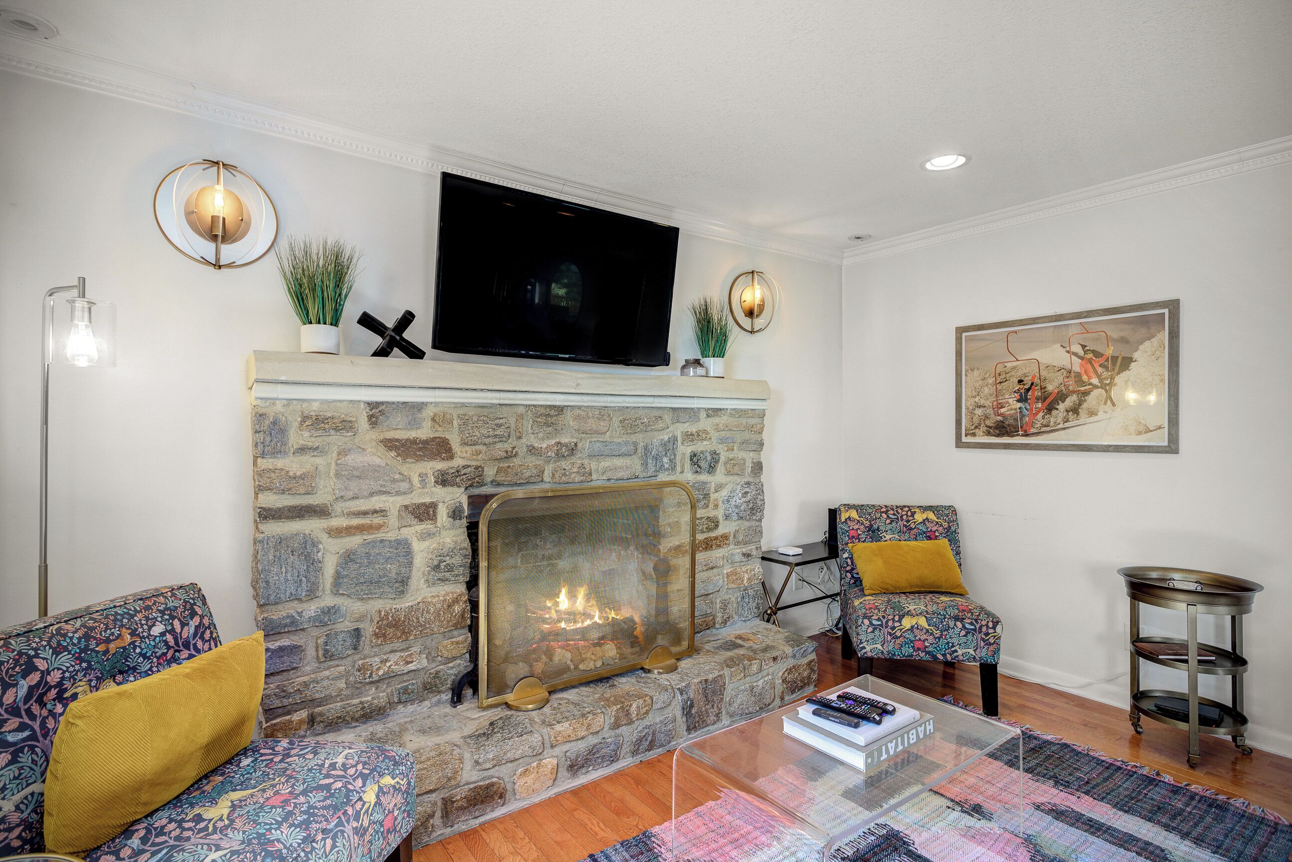 A living room with a stone fireplace, a flat-screen TV, patterned sofas, and a coffee table.