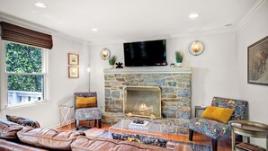 Una sala de estar con chimenea de piedra, sofá de cuero y sillones estampados.