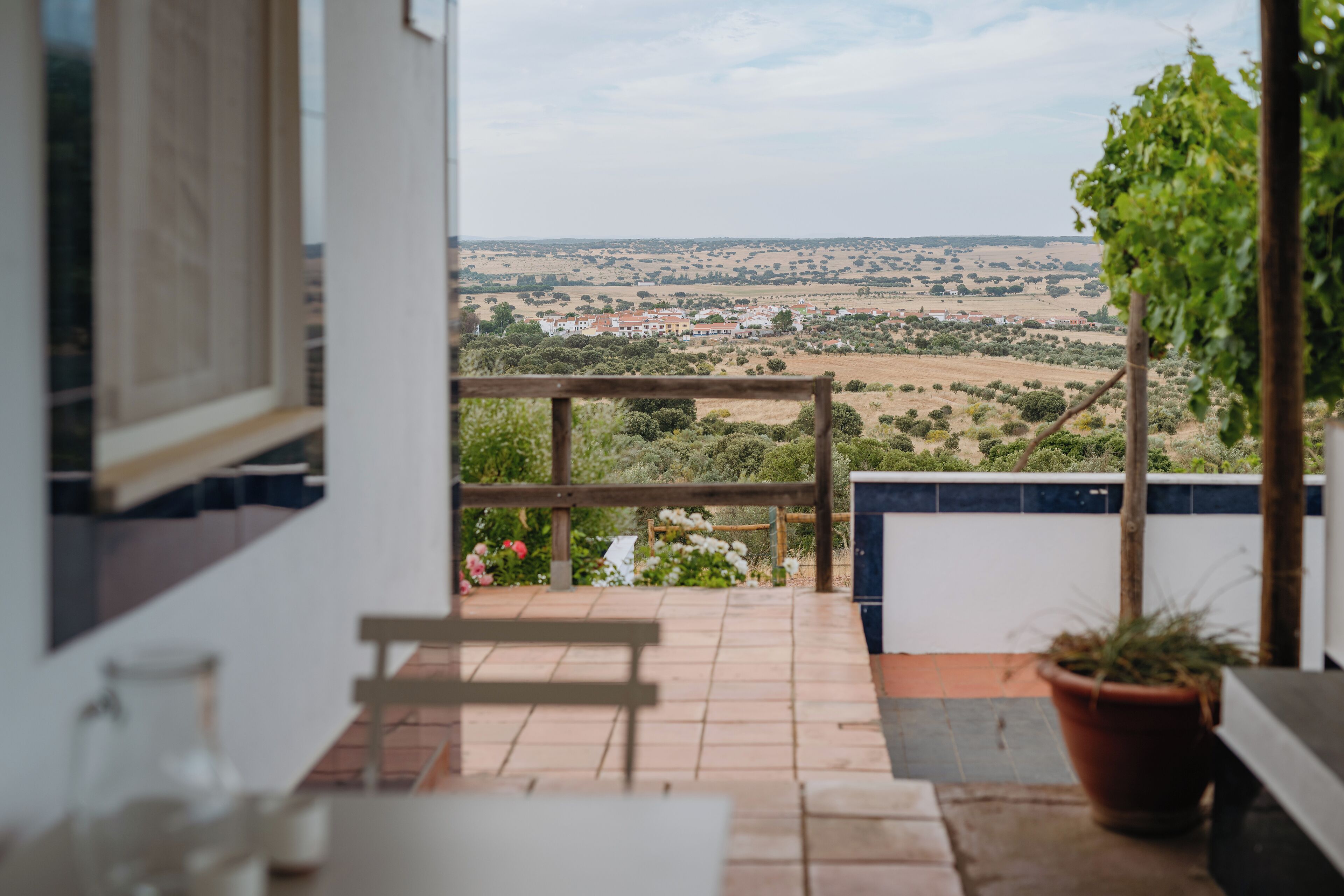 A balcony with a view of a rural landscape, a wooden bench, and a potted plant.