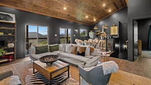 A modern living room with a large sectional sofa, a coffee table, and a fireplace. There are multiple windows offering a view of the outdoors.