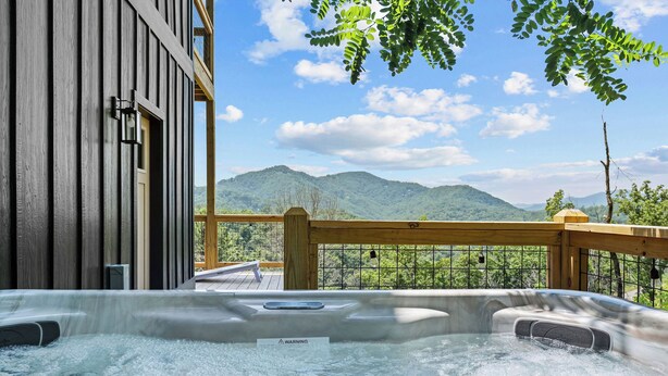 A hot tub with a wooden deck and a view of mountains.