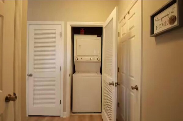 A laundry room with a washer and dryer, a door with a sign saying "Make yourself at HOME", and a door with a louvered design.
