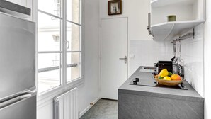 A compact kitchen with white cabinetry, a window, and a countertop with a fruit bowl. - Charming 1BR by Pompidou & Louvre - Sleeps 4 (Paris)
