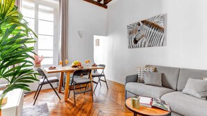 A modern living room with a herringbone floor, a grey sofa, a wooden dining table with chairs, and a large plant. - Charming 1BR by Pompidou & Louvre - Sleeps 4 (Paris)