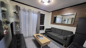 Moderni olohuone, jossa on sohva, sohvapöytä, televisio ja suuri peili.