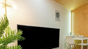 Une chambre moderne équipée d’un téléviseur à écran plat, d’une table à manger avec des chaises et d’une plante en pot.