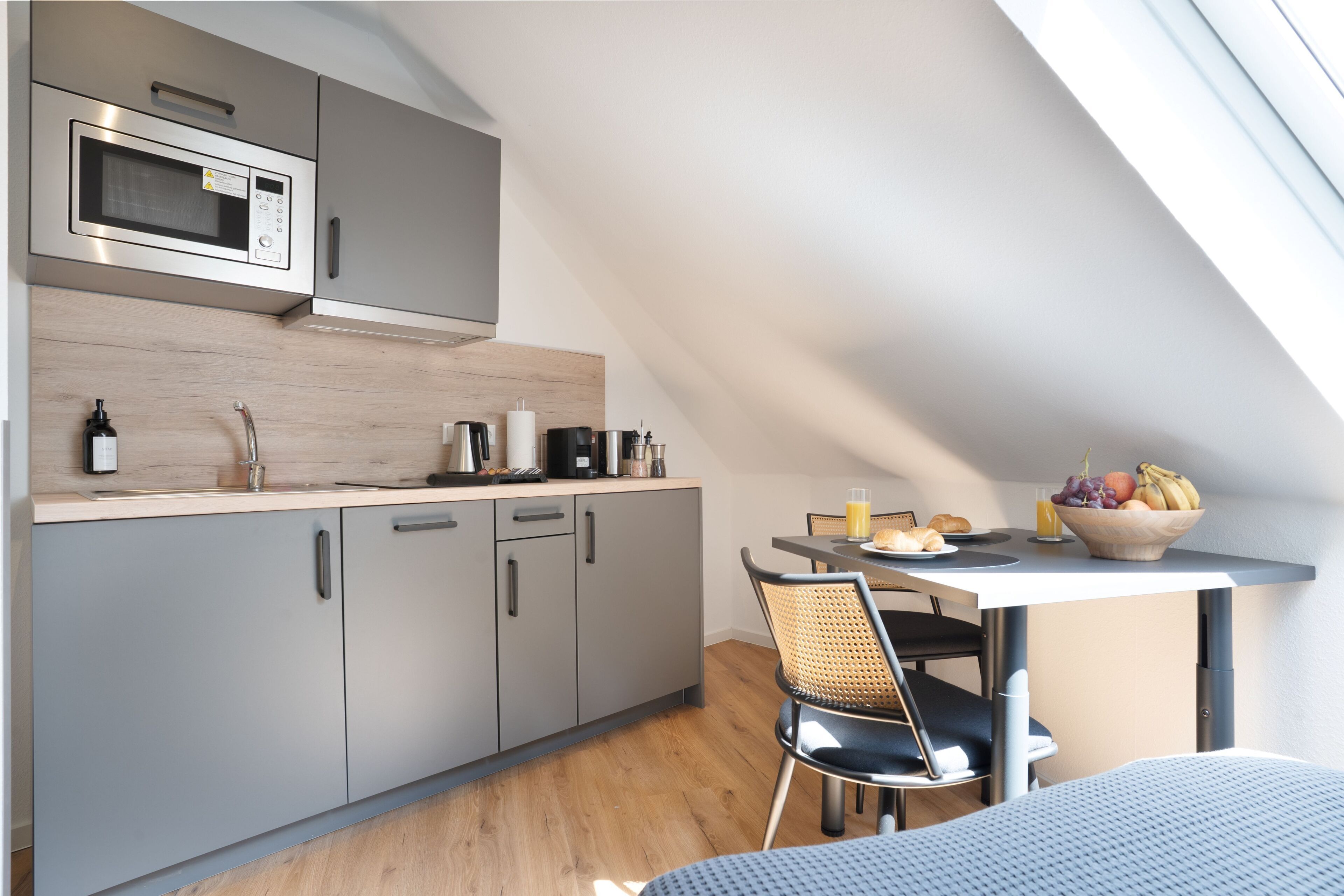 Une cuisine moderne avec des meubles de couleur grise, un four à micro-ondes et un coin repas comprenant une table et des chaises.