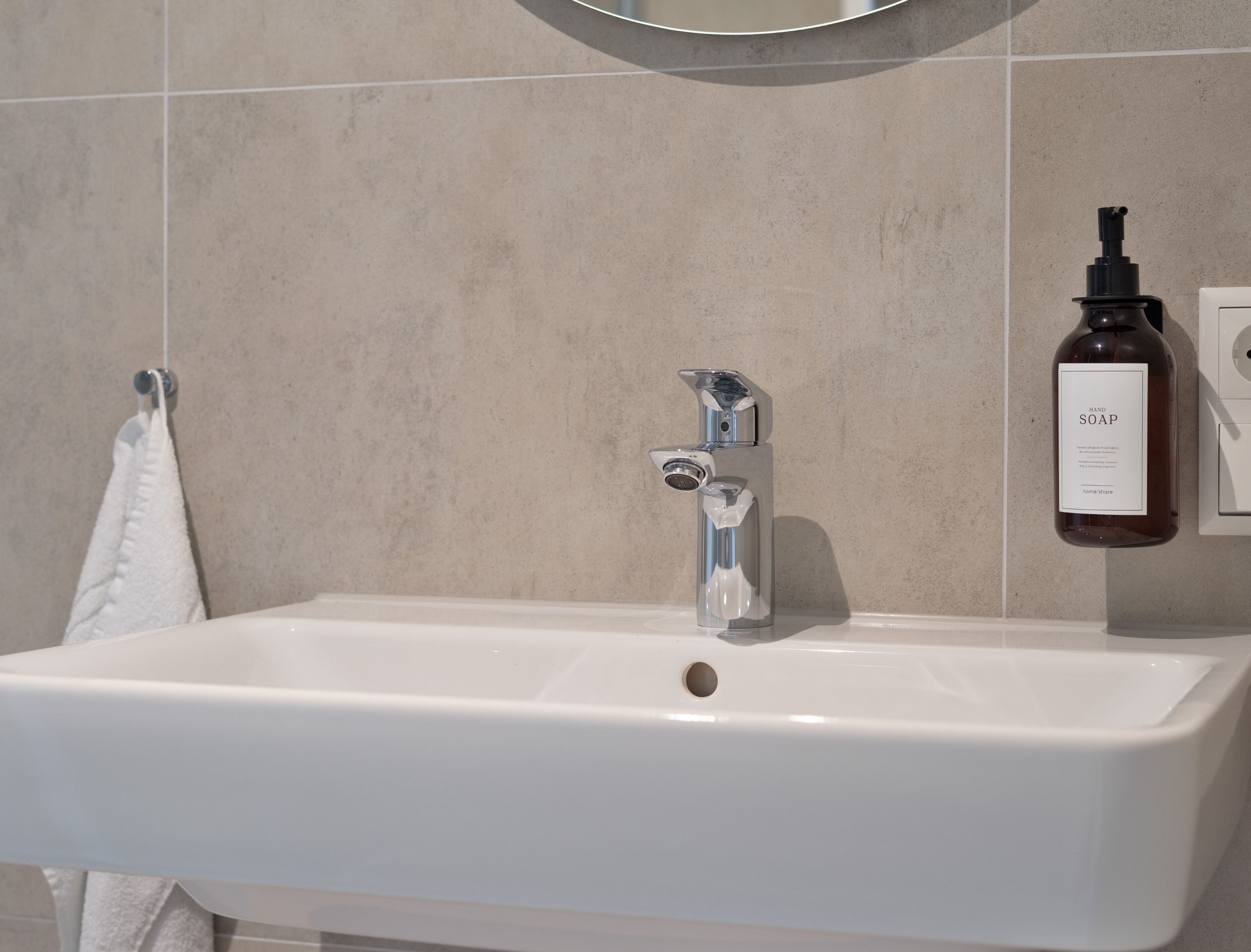 Une salle de bain avec un lavabo blanc, un robinet chromé et un flacon de savon liquide fixé au mur.