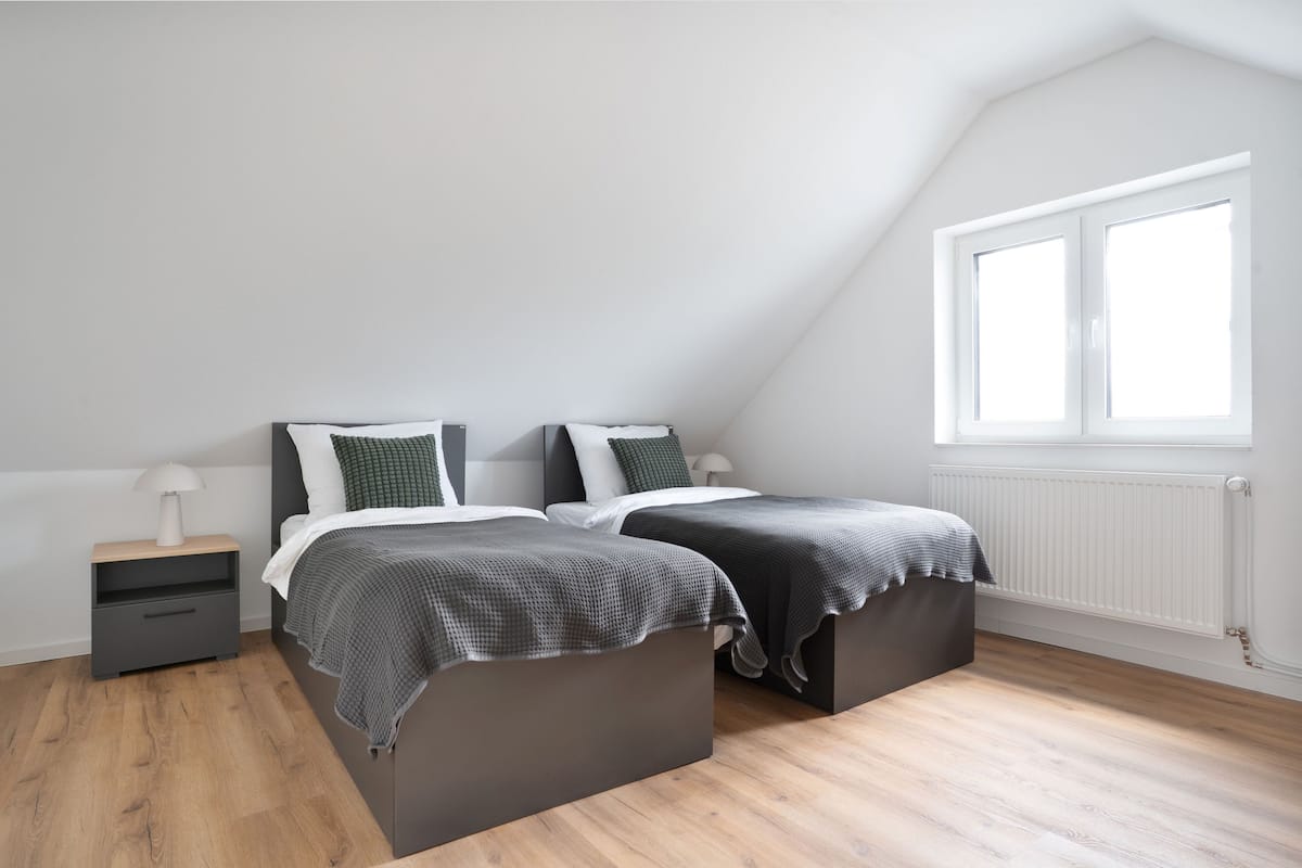 A bedroom with two beds, a nightstand, a lamp, and a window with blinds.