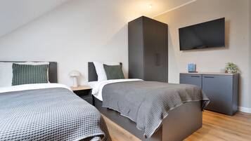Ein modernes Schlafzimmer mit zwei Betten, einem Fernseher und einem Kleiderschrank.