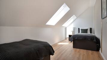 A bedroom with a sloped ceiling, skylights, a bed, a bedside table, and a nightstand.