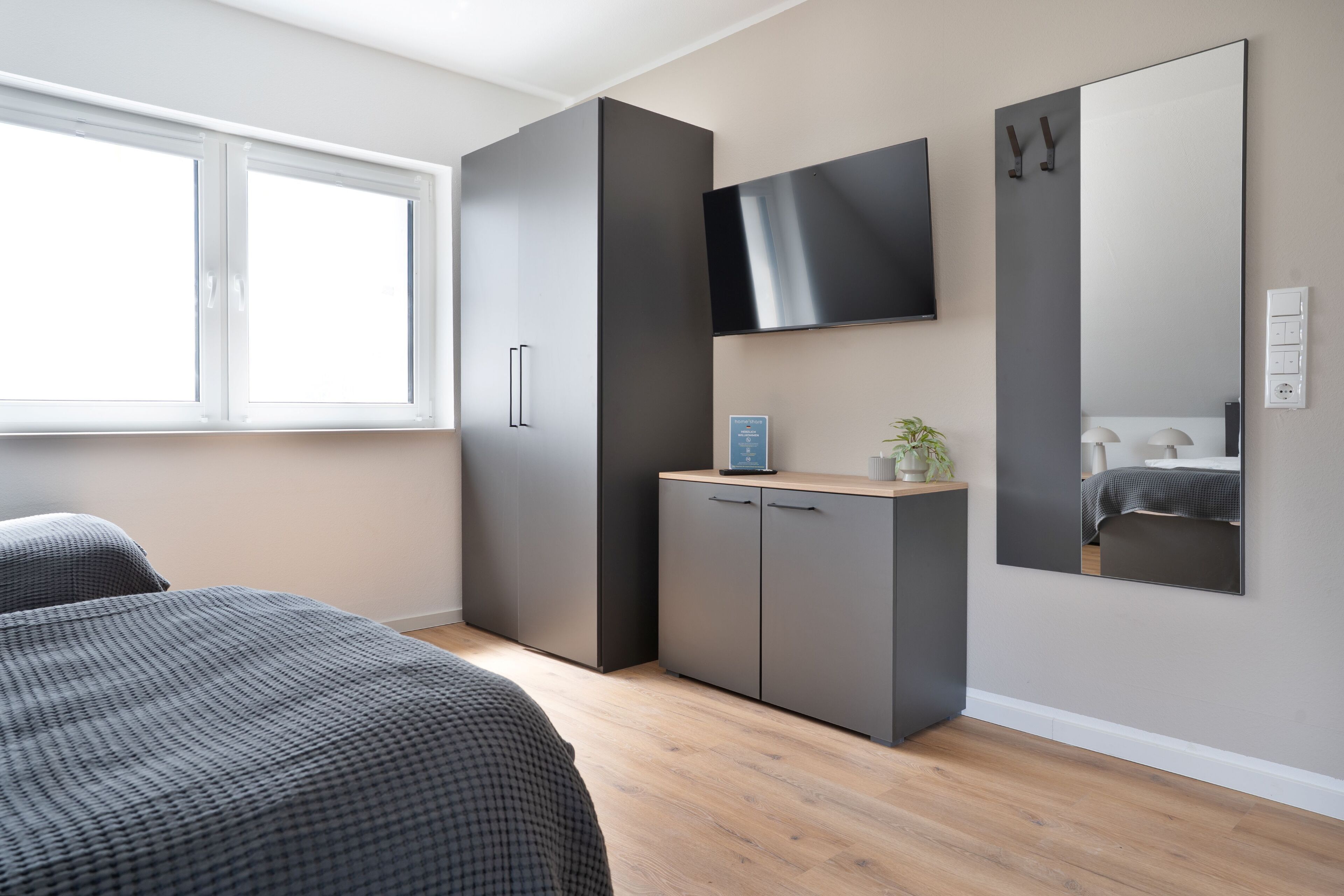 A bedroom with a bed, a wardrobe, a television, and a mirror.